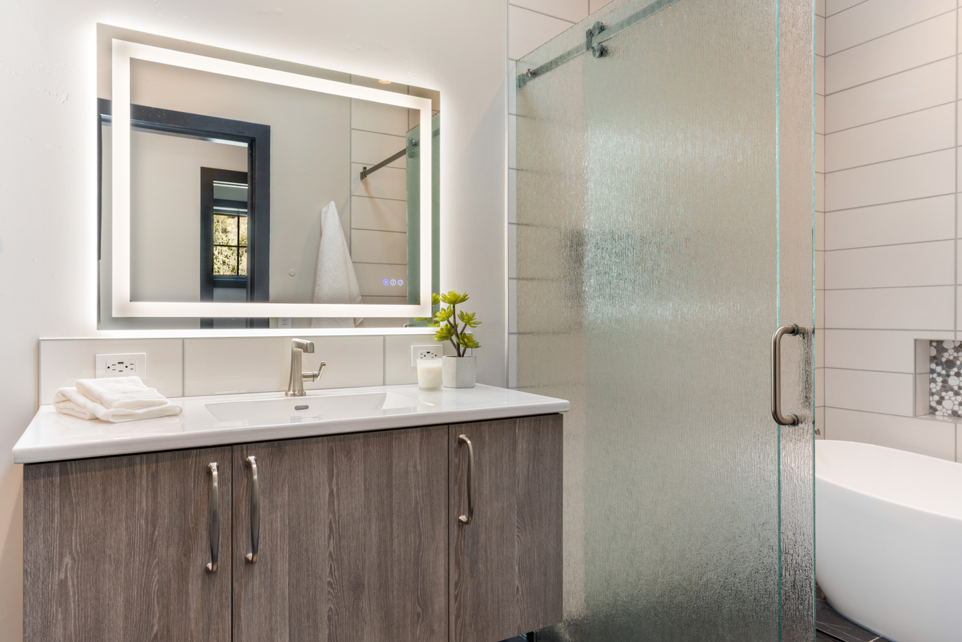 Guest bath with backlit mirror, glass shower, and soaking tub